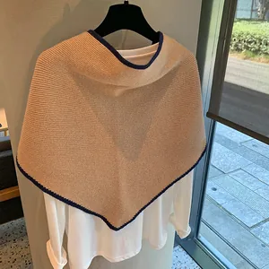 Detalle de chal de punto de lana caqui con ribete azul sobre una camiseta blanca