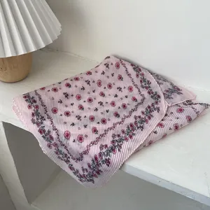 Detail of a pleated pink scarf with floral prints and wavy edges on a white desk