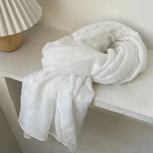 Detail showing white cotton linen shawl with delicate textured embroidery and fringe