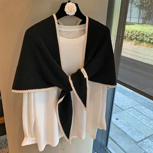 Detalle de la etiqueta 100% lana en un chal de punto negro con bordes blancos ondulados