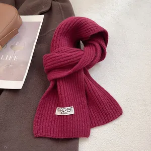 Detailed view of burgundy ribbed knit wool scarf featuring a woven minimalist brand tag