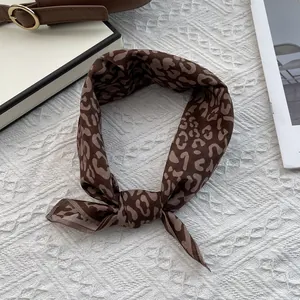 Detail of brown leopard print silk scarf tied in a knot on a quilted white backdrop