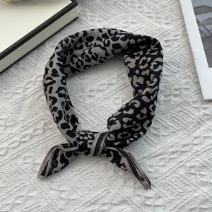 Close-up of leopard print silk scarf tied in a decorative knot on a textured white surface