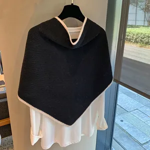 Detalle de chal triangular de lana negra con ribete blanco en una percha