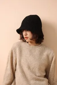 Detail of black merino wool knitted bucket hat showing intricate cable knit texture on woman