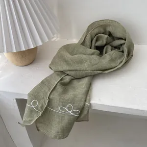 Close-up of light green linen scarf with delicate white spiral embroidery on edge