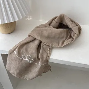 Detail of light brown scarf featuring delicate white embroidery and natural linen texture