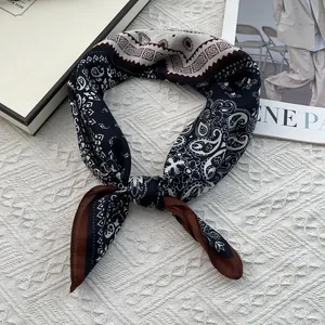 Detalle de un pañuelo de seda anudado con estampado paisley en azul marino y crema