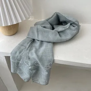 Detail of light blue linen scarf with delicate white vine embroidery and natural texture