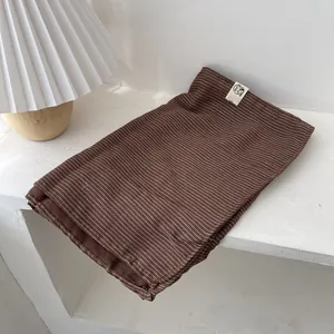 Gros plan d'une écharpe en lin marron rayée pliée avec une étiquette minimaliste
