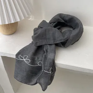 Detail of dark gray linen scarf showing delicate white embroidered linear bow patterns