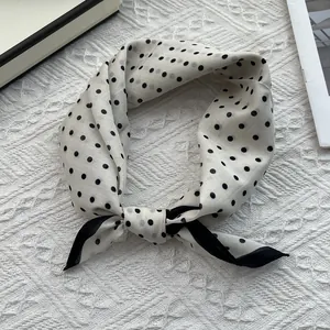 Detailed view of white polka dot silk scarf with black borders and knotted styling