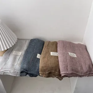 Detail of four knit cotton linen scarves showing grid texture and brand tags in soft tones