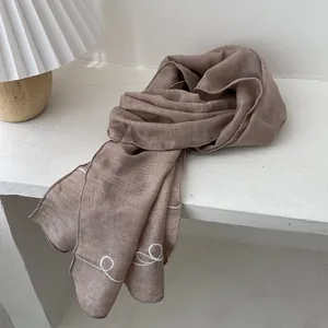 Detail of mocha cotton linen scarf featuring delicate white embroidered lines and textures