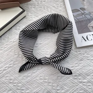 Detail of a black and white striped silk scarf tied in a bow on a white textured background