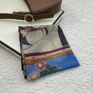 Detailed view of floral and bird print silk scarf placed on a gift box with a leather bag