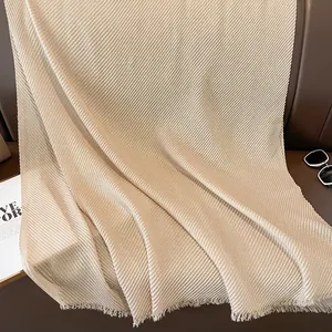 Detail of champagne gold pleated scarf with metallic luster and fringed edge on leather