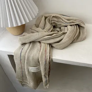 Close-up of beige linen scarf texture with subtle colored stripes and fabric label