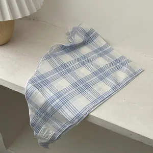 Blue and white checkered cotton scarf with small white fabric label on white surface