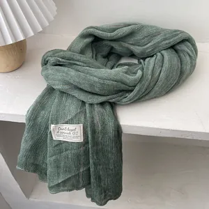 Detail of green linen scarf with textured stripes and woven label on white table