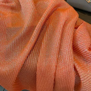 Detailed macro view of orange pleated linen scarf with gold foil shimmering texture