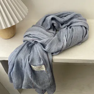 Detail view of light blue linen scarf texture with woven brand label on white surface