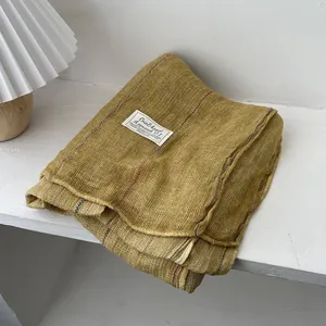 Detail of folded mustard yellow cotton linen scarf with woven label and striped edge