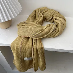 Close-up of textured yellow cotton linen scarf showing fabric weave and stitched brand label