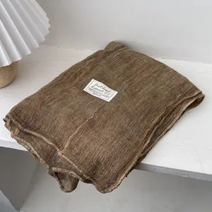Close-up of brown linen scarf with colorful stitching and fabric label on a white shelf