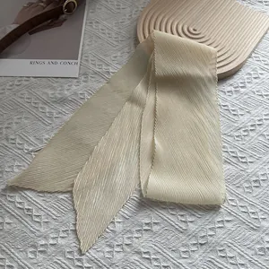 Detail eines plissierten beigen Schals auf Holztablett mit dekorativer Kunstkarte