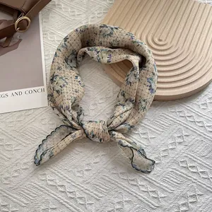 Macro detail of beige floral silk scarf showing delicate rhombus texture and dark piping edge