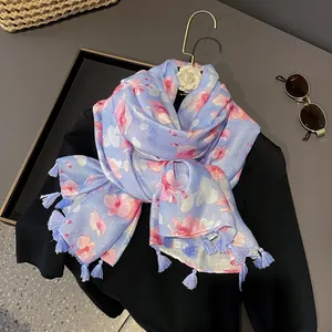Écharpe fleurie bleu clair avec fleurs roses et pompons suspendue à un cintre doré