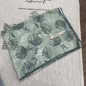 Close-up of light green floral linen scarf with lace edges and explore infinity tag