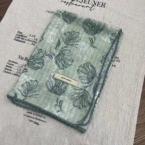 Detail of light green floral cotton linen scarf with hollow lace edge and brand tag