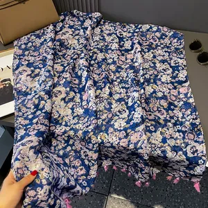 Floral print blue shawl with pink tassels on a table with sunglasses and handbag