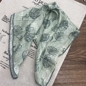 Close-up of light green floral silk scarf with crochet lace edges on linen fabric