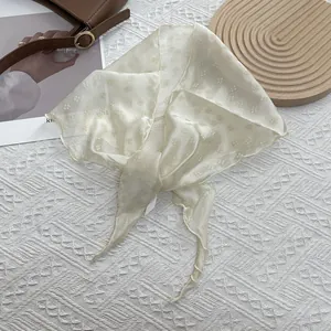 Élégant foulard en soie jacquard floral crème avec un sac marron sur un tapis tressé