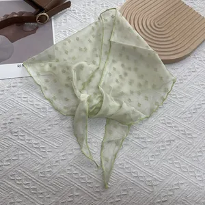 Détail d'un foulard triangle vert clair transparent avec flocage floral et bords ondulés