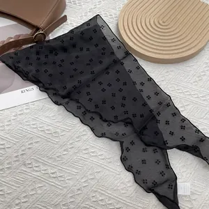Détail d'un foulard noir translucide avec motifs floraux et bordure ondulée chic