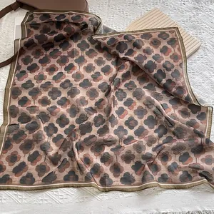 Detail of RINGS AND CONCH silk scarf with brown floral patterns and stitched edges