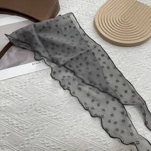 Détail d'un foulard en mousseline grise avec imprimé floral noir et bords ondulés