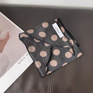 Detalle de un pañuelo de lino con lunares y etiqueta tejida sobre fondo de cuero
