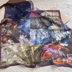 Detailed close-up of a floral silk square scarf with vibrant botanical prints and purple edges