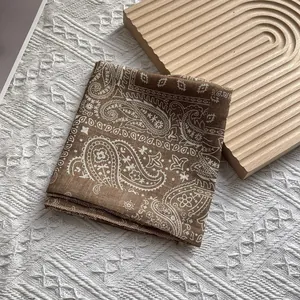Gros plan d'un foulard carré marron à motif paisley montrant la texture fine du coton