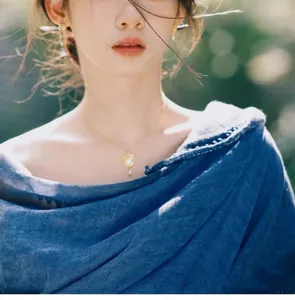 Détail d'un collier avec disque doré et perle porté sur une chemise en lin bleu