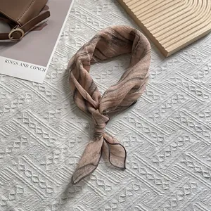 Detail eines Seidenschals mit braunem Batikmuster, elegant geknotet auf weißem Grund