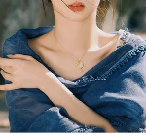 Détail du collier doré avec pendentif feuille et perle porté sur une écharpe en lin