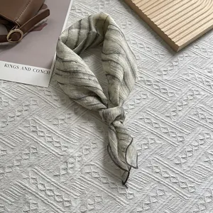 Detailaufnahme des geknoteten Seidentuchs mit grauen Batikstreifen auf cremeweißem Grund