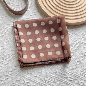 Vintage brown silk scarf with white polka dots placed on a white textured background