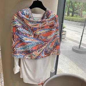 Close-up of lightweight paisley printed shawl styled over a white top on a hanger